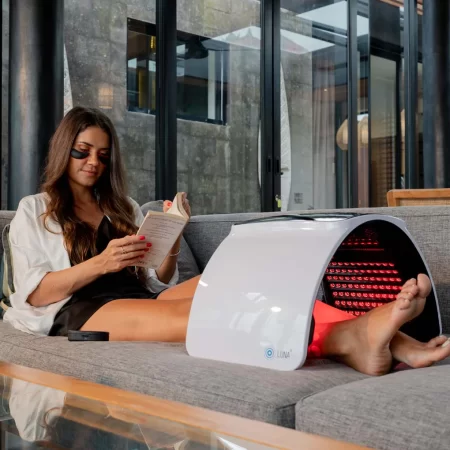 Woman relaxing with a book while using a red light therapy device for foot care.