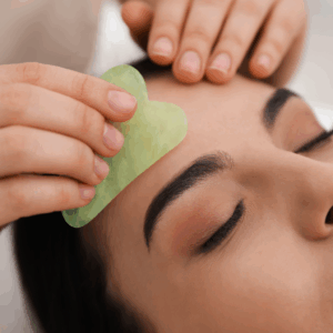 Woman receiving facial treatment with jade gua sha tool at a spa.