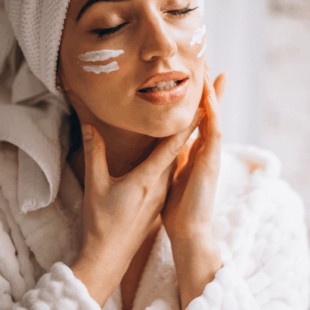 Woman applying facial cream in a cozy spa robe, enjoying a skincare routine.