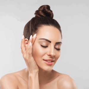 A relaxed woman with a bun holds her face, showcasing healthy skin and serene beauty.