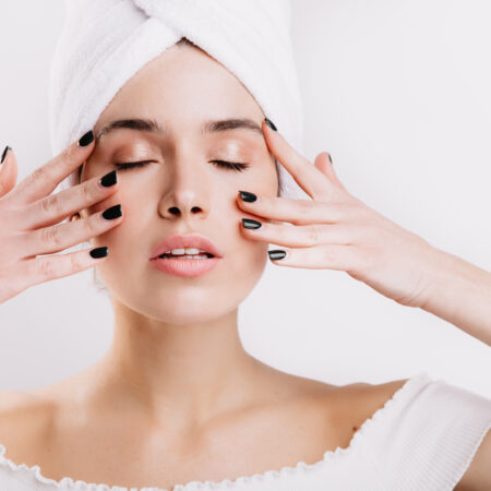 Woman relaxing with closed eyes, hands on face, and a towel on her head in a serene spa setting.