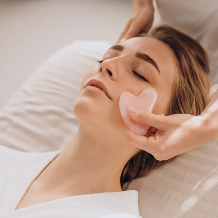 A spa treatment with a woman receiving a gentle facial massage using a rose quartz gua sha tool.